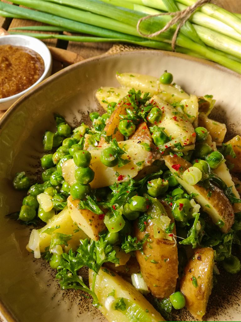 Ein Teller mit Kartoffel-Erbsen-Salat. Im Hintergrund sind ein paar Lauchzwiebeln.