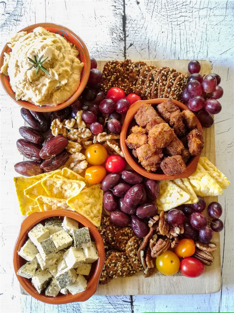 Vegane Tapasplatte mit vielen Leckereien: Weintrauben, Kräckern, Maistortillas, Nüssen, Tofuwürfeln, Bohnendip